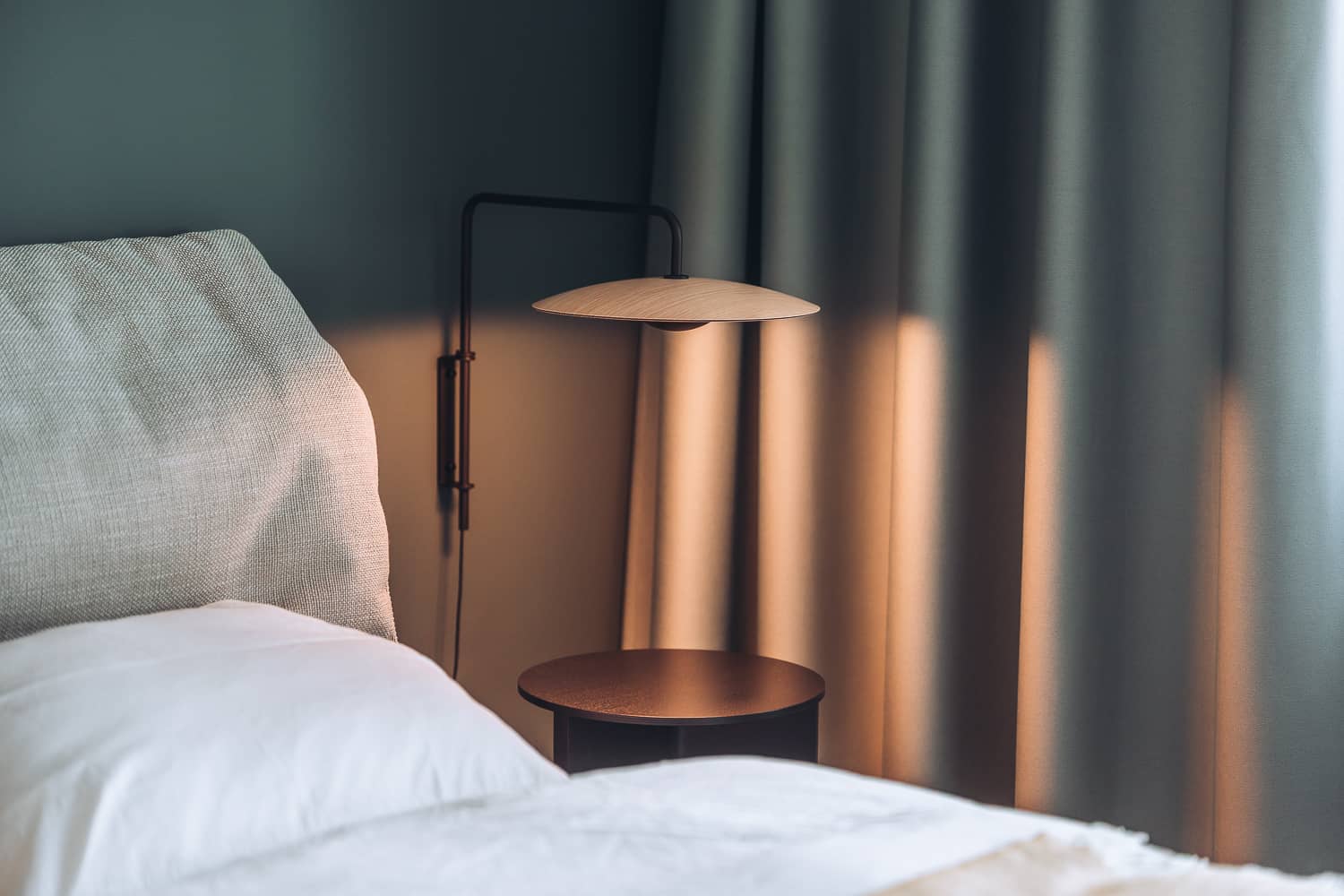 Neben einem Bett steht ein Nachttisch, welcher mit stimmungsvollem Licht beleuchtet wird